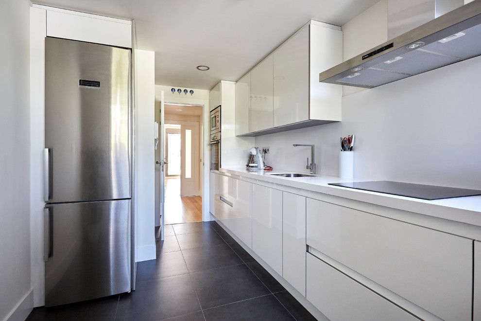 Design ideas for a mid-sized modern single-wall separate kitchen in Madrid with flat-panel cabinets, white cabinets, white splashback, stainless steel appliances, white benchtop, an undermount sink, black floor, concrete floors and no island.