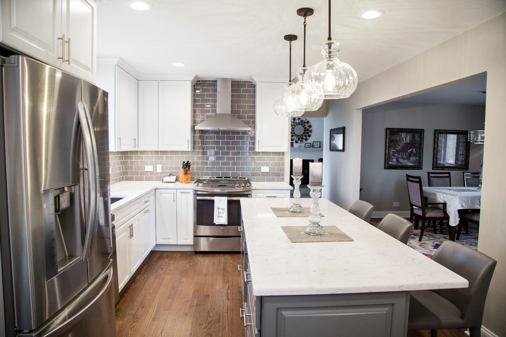 Eat-in kitchen - mid-sized transitional l-shaped medium tone wood floor and brown floor eat-in kitchen idea in Chicago with an undermount sink, raised-panel cabinets, white cabinets, quartz countertops, gray backsplash, ceramic backsplash, stainless steel appliances, an island and white countertops