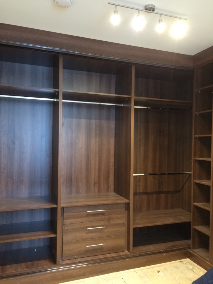Mid-sized contemporary gender-neutral built-in wardrobe in London with glass-front cabinets, dark wood cabinets and light hardwood floors.
