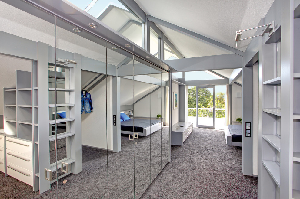 This is an example of a large contemporary gender-neutral dressing room in Stuttgart with glass-front cabinets, carpet and grey floor.