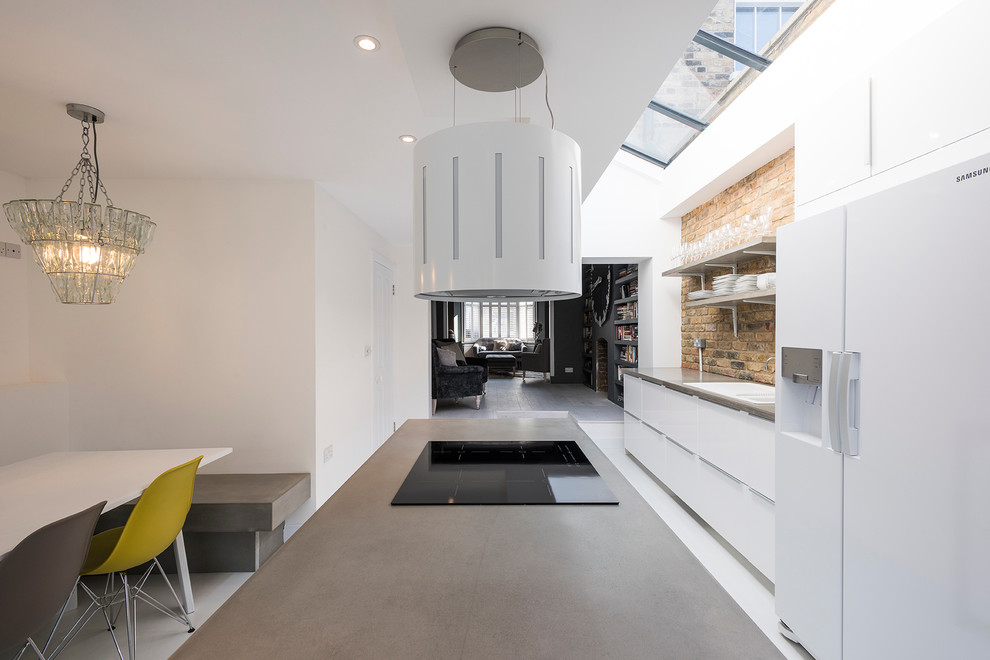 Design ideas for a large transitional open plan kitchen in London with a drop-in sink, flat-panel cabinets, white cabinets, granite benchtops, yellow splashback, white appliances, concrete floors and with island.