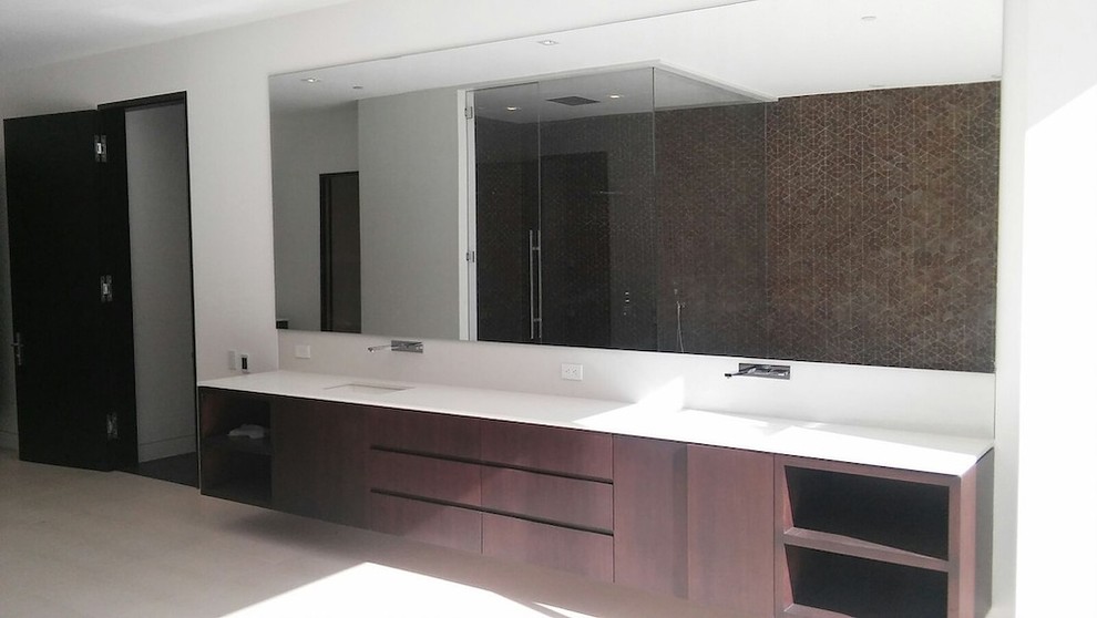 This is an example of a large modern 3/4 bathroom in Los Angeles with flat-panel cabinets, dark wood cabinets, a corner shower, a one-piece toilet, brown tile, porcelain tile, white walls, limestone floors, an undermount sink and engineered quartz benchtops.