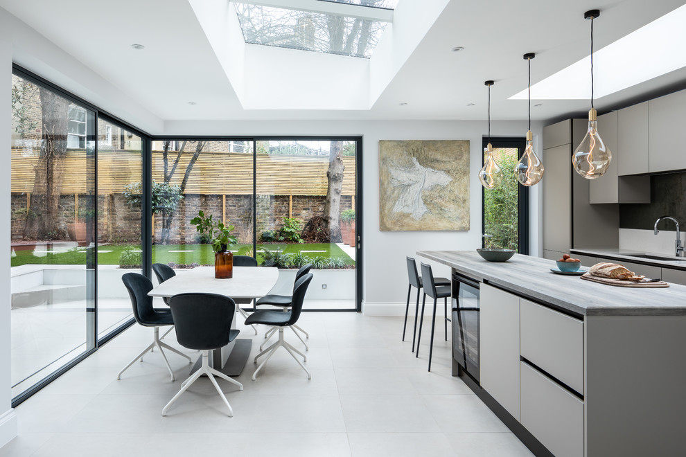Photo of a contemporary eat-in kitchen in London with an undermount sink, flat-panel cabinets, grey cabinets, with island, beige floor and white benchtop.