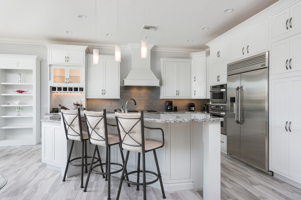 This is an example of a mid-sized transitional l-shaped open plan kitchen in Phoenix with shaker cabinets, white cabinets, grey splashback, subway tile splashback, stainless steel appliances, light hardwood floors and with island.
