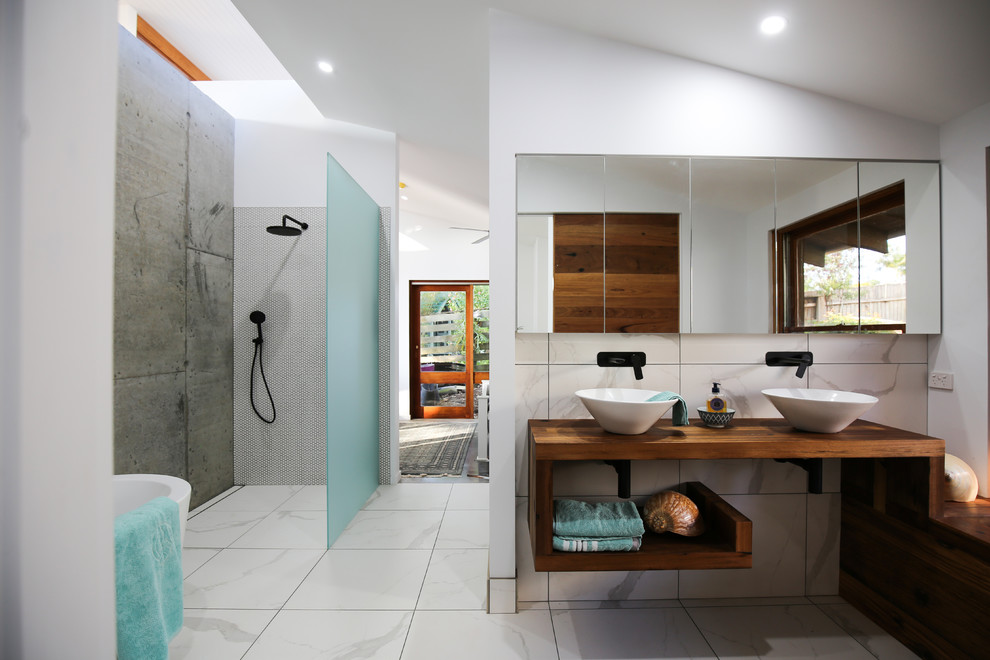 Design ideas for a beach style master bathroom in Wollongong with open cabinets, medium wood cabinets, a freestanding tub, a corner shower, gray tile, mosaic tile, white walls, a vessel sink, wood benchtops, grey floor, an open shower and brown benchtops.