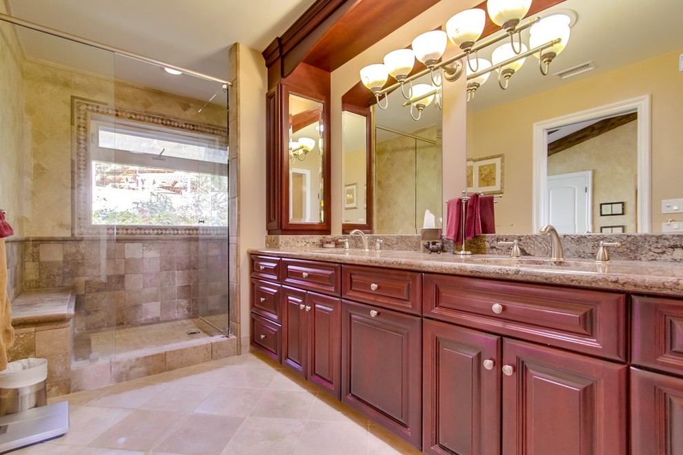 Photo of a mid-sized mediterranean master bathroom in Los Angeles with raised-panel cabinets, red cabinets, an alcove shower, a two-piece toilet, beige tile, terra-cotta tile, an undermount sink, granite benchtops, beige walls, limestone floors and a hinged shower door.