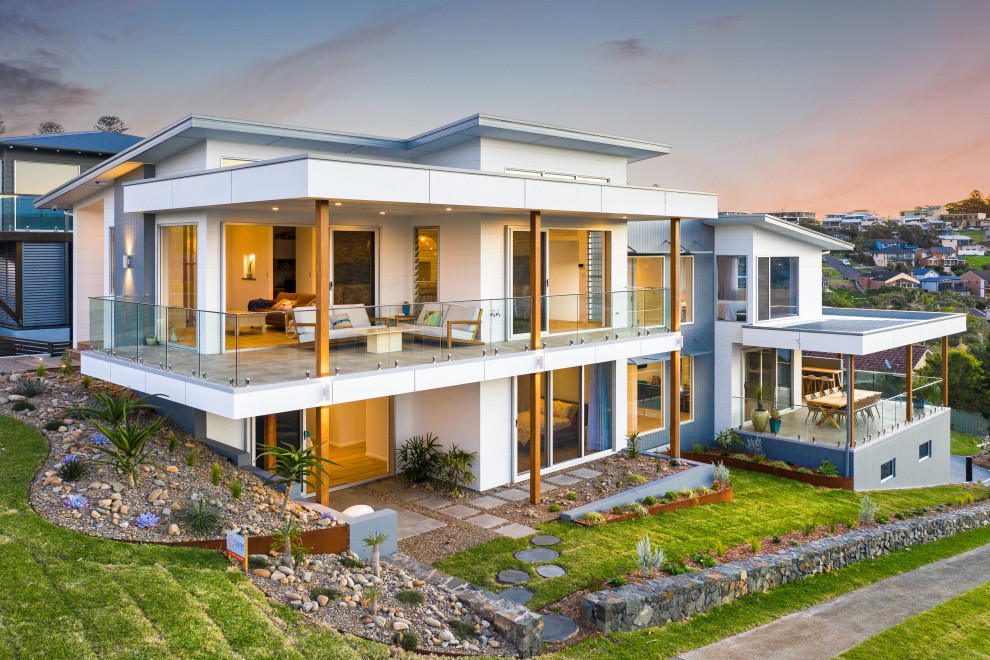 Photo of an expansive beach style split-level beige house exterior in Wollongong with mixed siding, a flat roof and a metal roof.