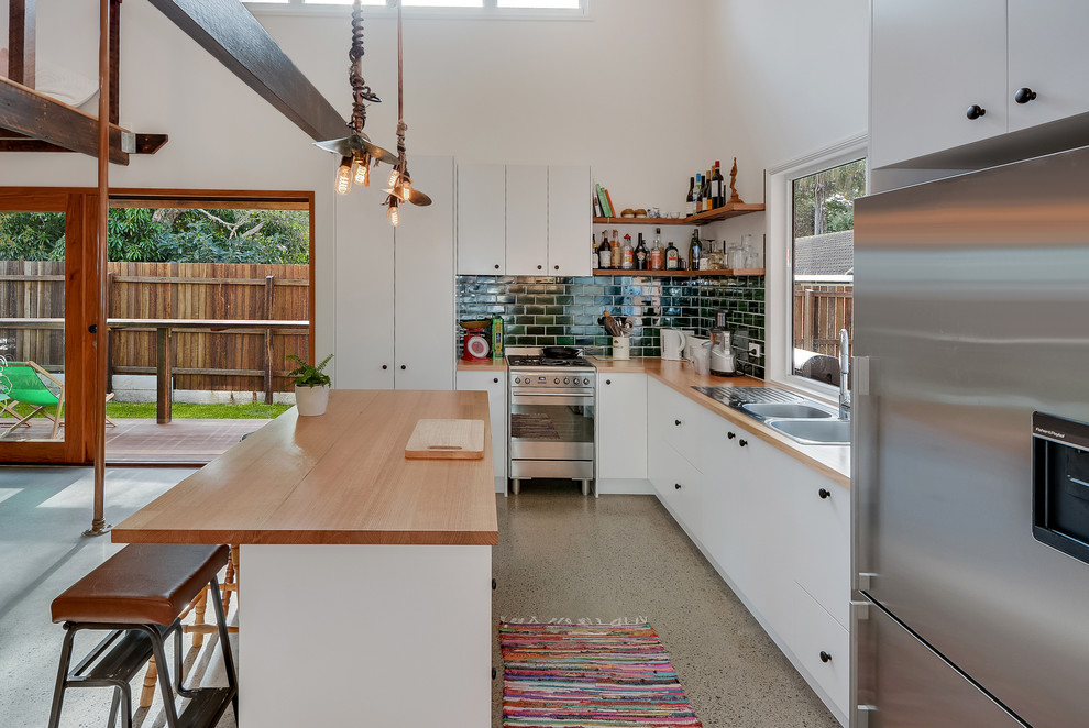Industrial l-shaped open plan kitchen in Sunshine Coast with a double-bowl sink, flat-panel cabinets, white cabinets, wood benchtops, green splashback, subway tile splashback, stainless steel appliances and with island.