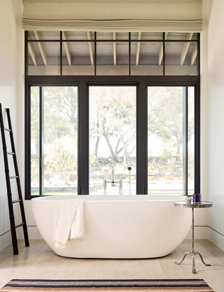This is an example of a country master bathroom in San Francisco with a freestanding tub, white walls and beige floor.