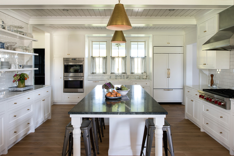 Inspiration for a country u-shaped kitchen in Minneapolis with a farmhouse sink, shaker cabinets, white splashback, subway tile splashback, panelled appliances, medium hardwood floors, with island and brown floor.