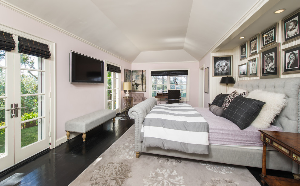 This is an example of a large transitional bedroom in Los Angeles with pink walls and dark hardwood floors.
