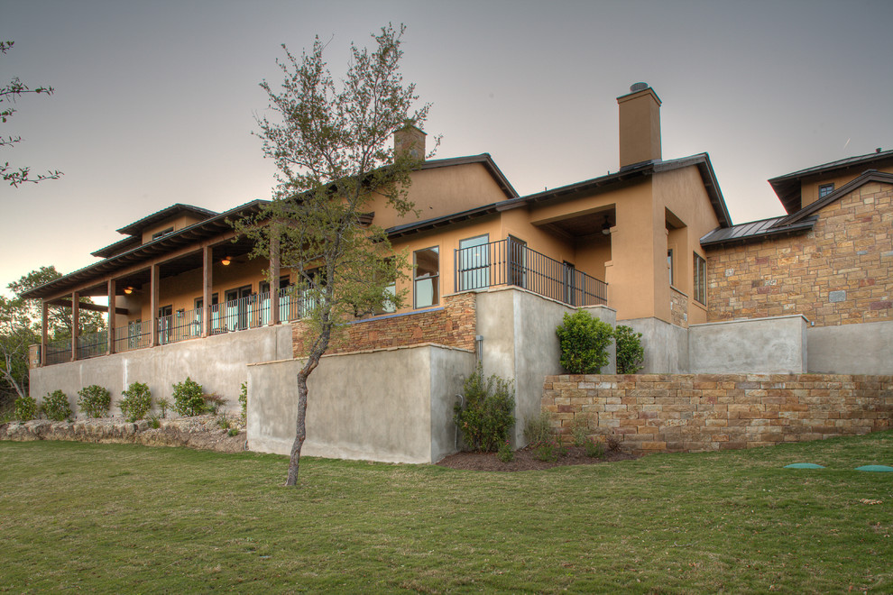 This is an example of a large traditional split-level beige house exterior in Austin with stone veneer, a gable roof and a metal roof.