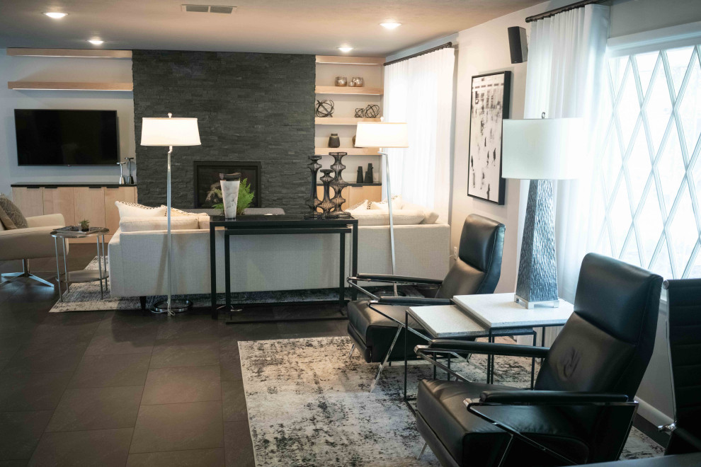 Aménagement d'un grand salon rétro ouvert avec un mur gris, un sol en vinyl, une cheminée standard, un manteau de cheminée en pierre et un sol noir.