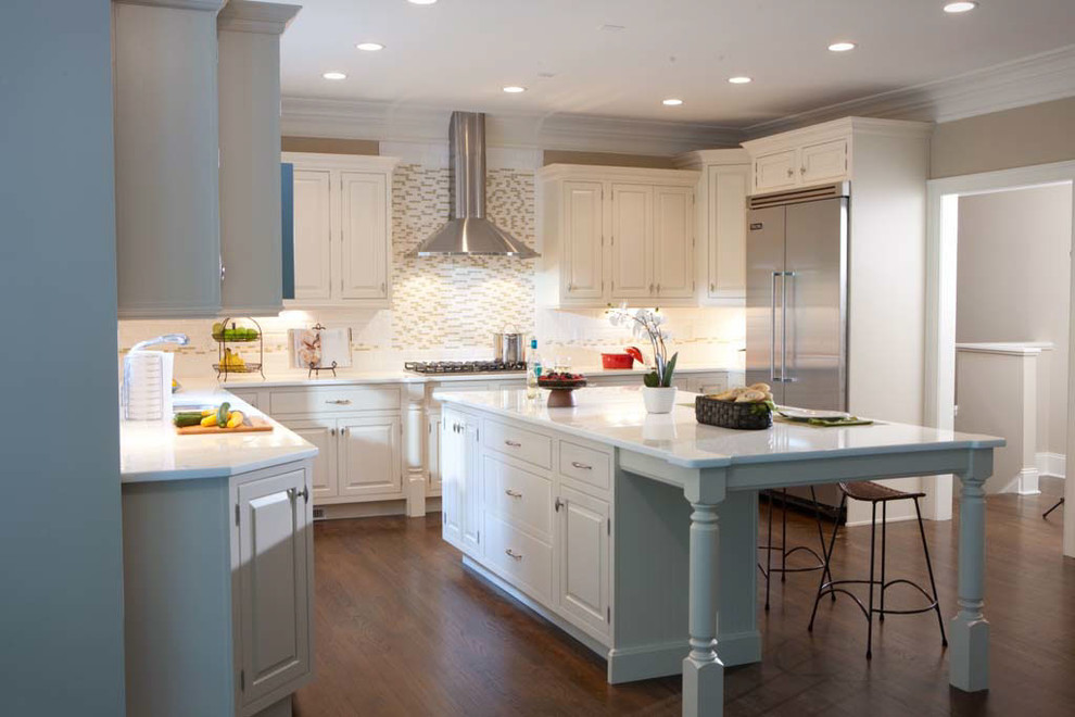Example of a large transitional l-shaped dark wood floor and brown floor eat-in kitchen design with a drop-in sink, raised-panel cabinets, white cabinets, solid surface countertops, white backsplash, ceramic backsplash, stainless steel appliances and an island