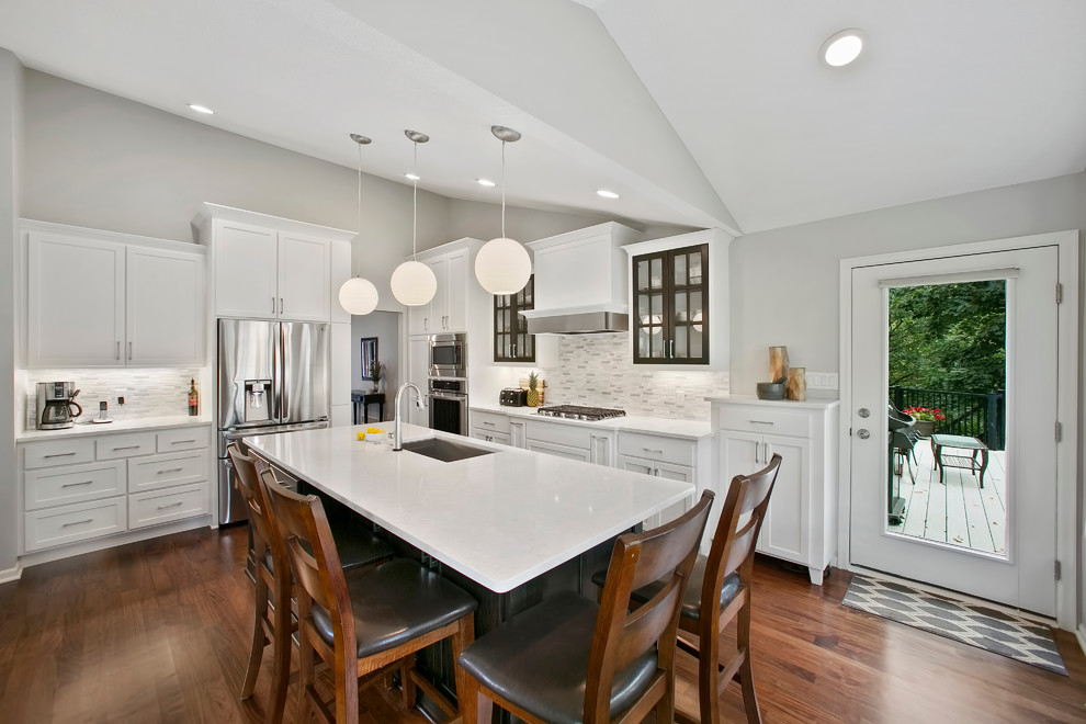 Transitional medium tone wood floor kitchen photo in Minneapolis with an undermount sink, flat-panel cabinets, white cabinets, quartz countertops, white backsplash, mosaic tile backsplash, stainless steel appliances and an island