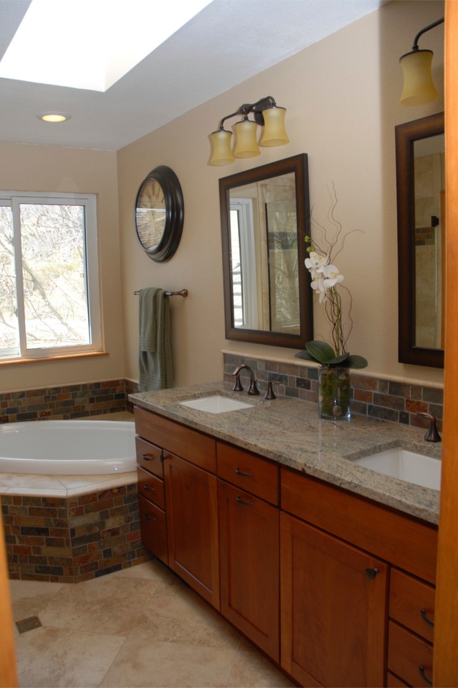 Photo of a transitional bathroom in Denver with an undermount sink, shaker cabinets, medium wood cabinets, granite benchtops, a drop-in tub, a corner shower, beige tile, stone tile, beige walls and travertine floors.