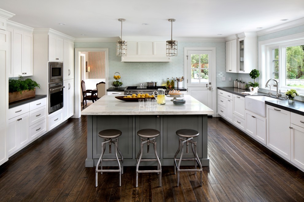 Transitional u-shaped kitchen in San Francisco with a farmhouse sink, shaker cabinets, white cabinets, blue splashback, glass tile splashback, stainless steel appliances, dark hardwood floors and with island.