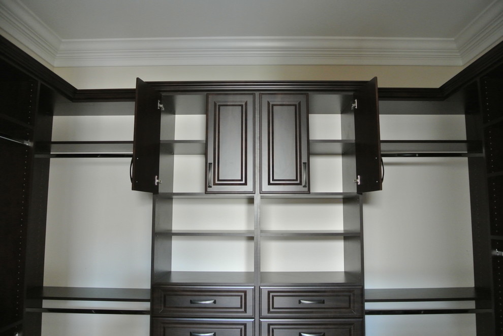 This is an example of a large traditional gender neutral walk-in wardrobe in Miami with raised-panel cabinets, dark wood cabinets and travertine flooring.