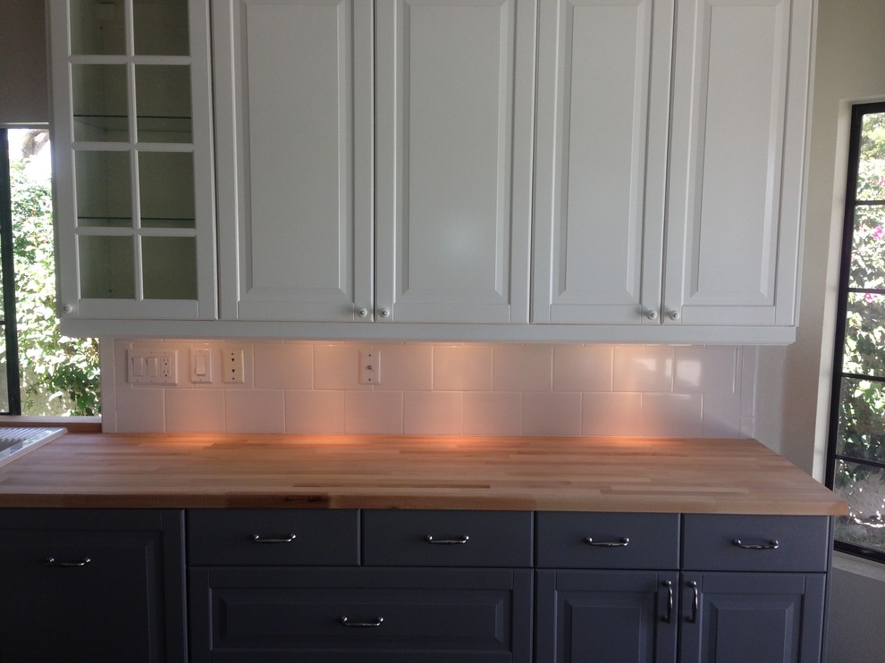 Kitchen - transitional laminate floor and brown floor kitchen idea with a farmhouse sink, shaker cabinets, white cabinets, wood countertops, white backsplash, subway tile backsplash, stainless steel appliances and brown countertops