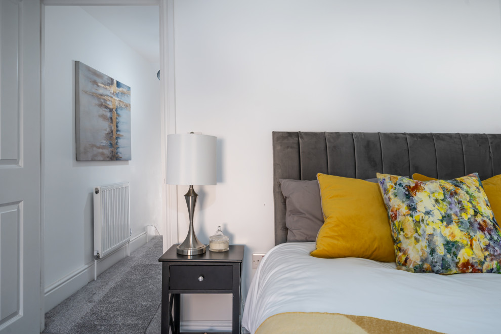 Medium sized contemporary guest and grey and yellow bedroom in London with white walls, carpet and grey floors.