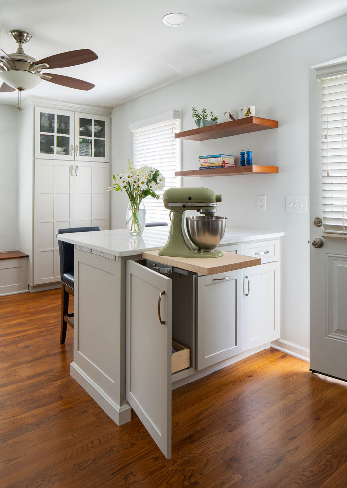 Imagen de cocina clásica pequeña con fregadero bajoencimera, armarios estilo shaker, puertas de armario blancas, encimera de cuarzo compacto, salpicadero azul, salpicadero de azulejos de cerámica, electrodomésticos de acero inoxidable, suelo de madera en tonos medios, península, suelo marrón y encimeras blancas