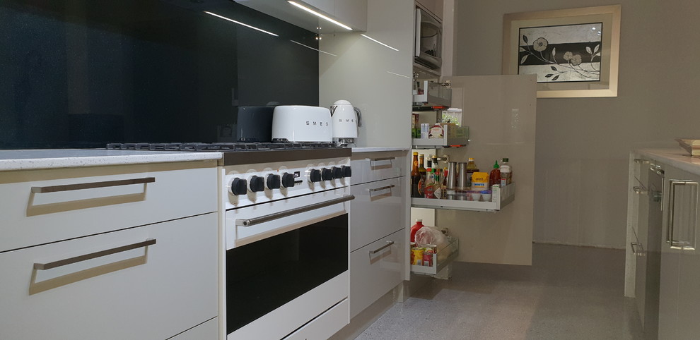 Mid-sized contemporary galley eat-in kitchen in Perth with a double-bowl sink, glass-front cabinets, beige cabinets, quartz benchtops, black splashback, glass sheet splashback, stainless steel appliances, concrete floors, with island, grey floor and white benchtop.