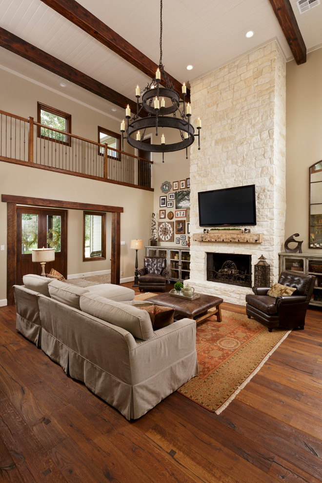 Inspiration for a large mediterranean living room in Houston with beige walls, dark hardwood floors, a standard fireplace, a stone fireplace surround and a wall-mounted tv.