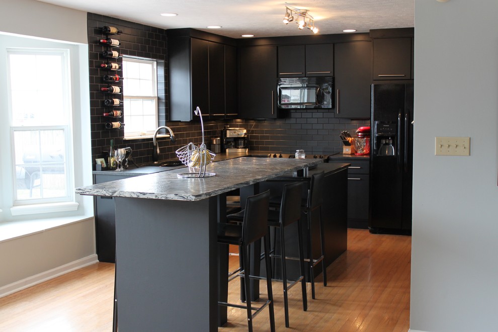 Design ideas for a mid-sized contemporary l-shaped eat-in kitchen in Indianapolis with an undermount sink, flat-panel cabinets, black cabinets, granite benchtops, black splashback, subway tile splashback, black appliances, medium hardwood floors and with island.