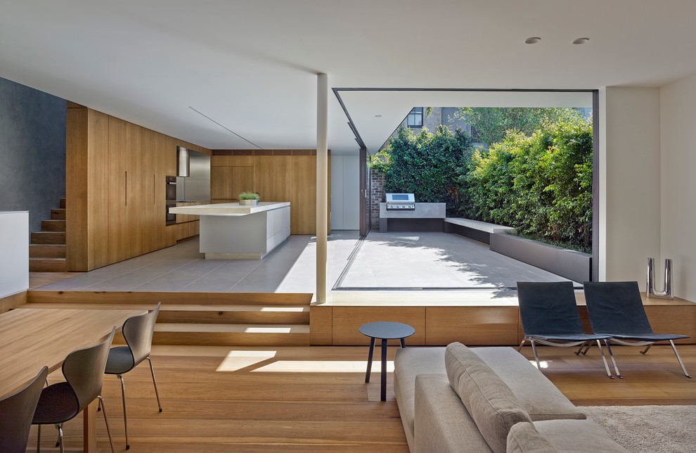 This is an example of a modern l-shaped open plan kitchen in Sydney with flat-panel cabinets, medium wood cabinets, panelled appliances, light hardwood floors and with island.