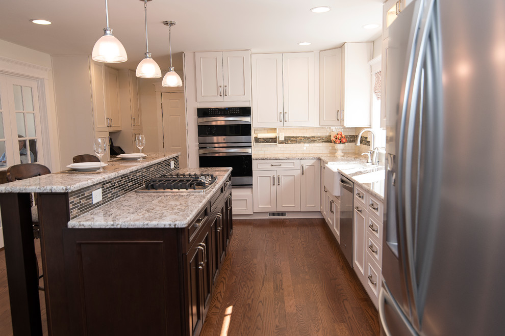 Large transitional l-shaped eat-in kitchen in Baltimore with a farmhouse sink, shaker cabinets, white cabinets, granite benchtops, white splashback, glass tile splashback, stainless steel appliances, medium hardwood floors, with island and brown floor.