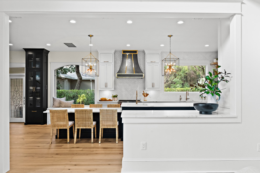 Large transitional u-shaped light wood floor kitchen photo with an undermount sink, shaker cabinets, white cabinets, quartz countertops, white backsplash, marble backsplash, paneled appliances, two islands and white countertops