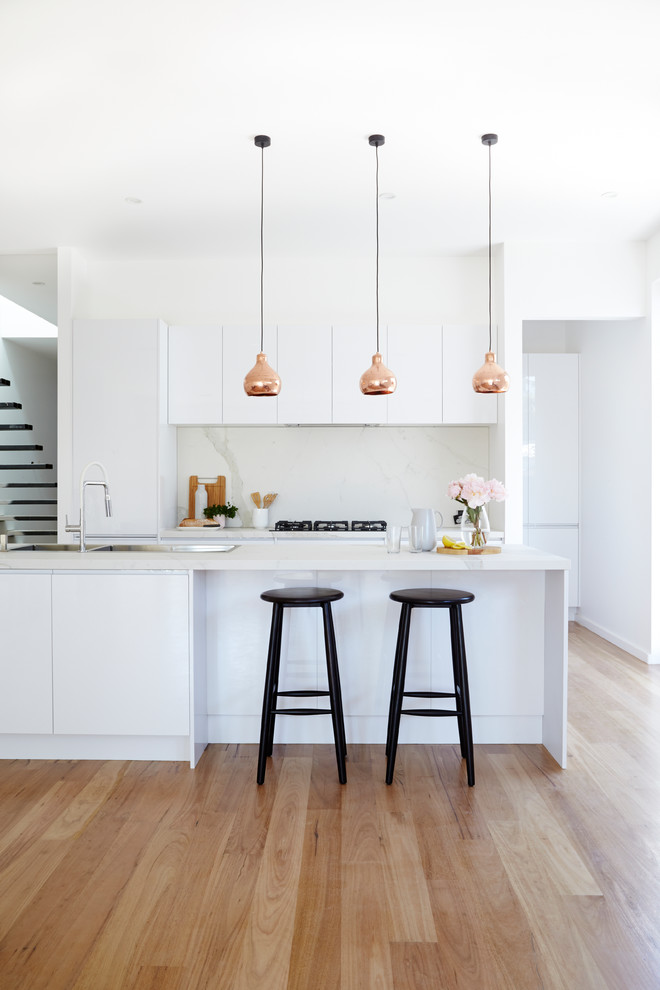 Inspiration for a modern galley kitchen pantry in Melbourne with white cabinets, marble benchtops, white splashback, stone slab splashback and with island.