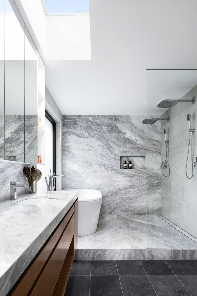 Example of a large trendy master gray tile and marble tile porcelain tile and double-sink bathroom design in Melbourne with flat-panel cabinets, medium tone wood cabinets, a wall-mount toilet, gray walls, an undermount sink, marble countertops, a niche and a floating vanity