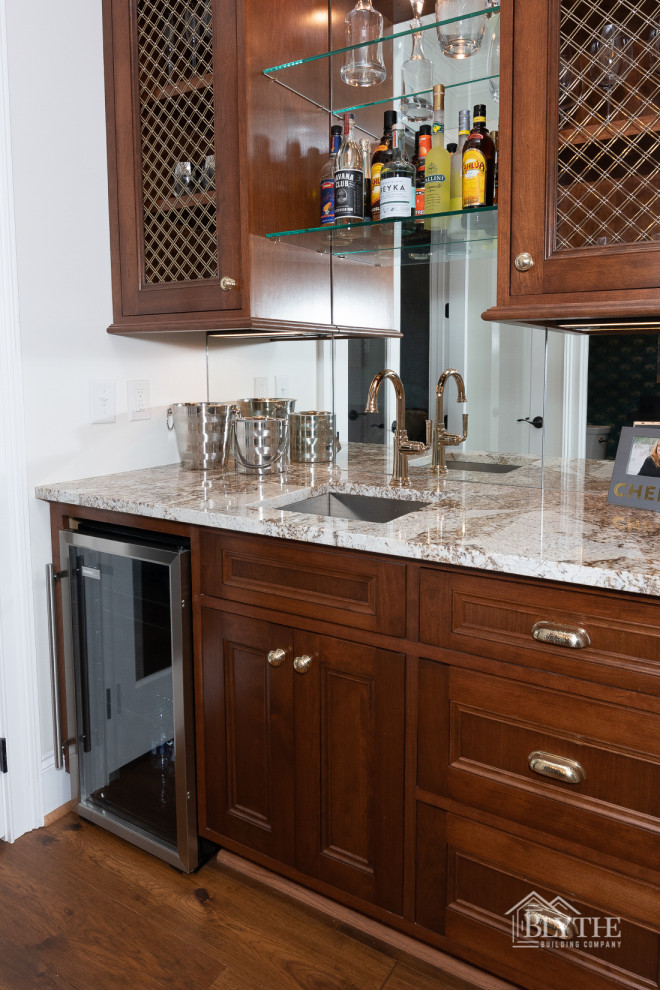 Photo of a large arts and crafts wet bar in Other with an undermount sink, glass-front cabinets, dark wood cabinets, granite benchtops, dark hardwood floors, brown floor and multi-coloured benchtop.