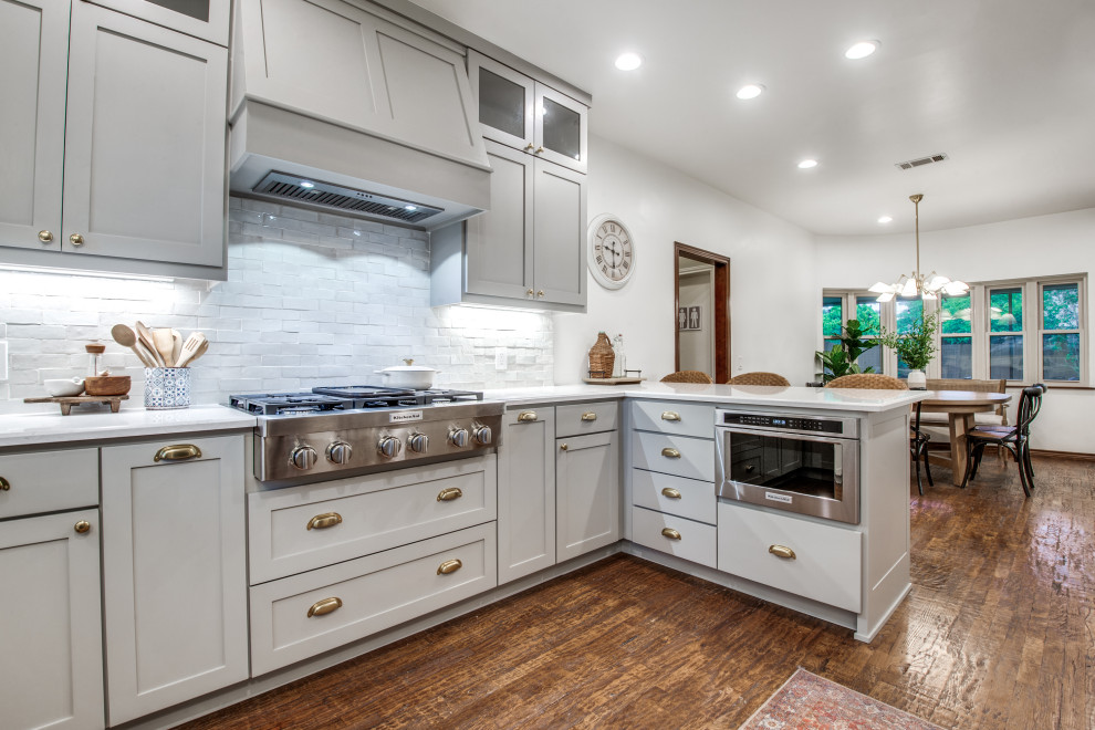 Medium sized traditional grey and white enclosed kitchen in Dallas with a belfast sink, shaker cabinets, grey cabinets, composite countertops, white splashback, cement tile splashback, stainless steel appliances, dark hardwood flooring, a breakfast bar, brown floors, grey worktops and feature lighting.