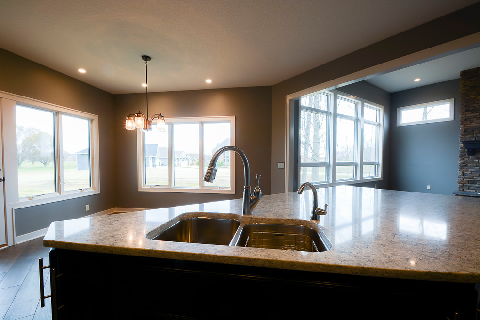 Example of a large transitional l-shaped dark wood floor and brown floor open concept kitchen design with a double-bowl sink, shaker cabinets, black cabinets, gray backsplash, stainless steel appliances and an island