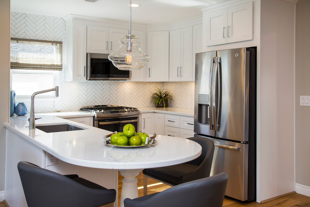 Inspiration for a small transitional u-shaped open plan kitchen in San Diego with an undermount sink, shaker cabinets, white cabinets, quartz benchtops, white splashback, ceramic splashback, stainless steel appliances, medium hardwood floors and a peninsula.