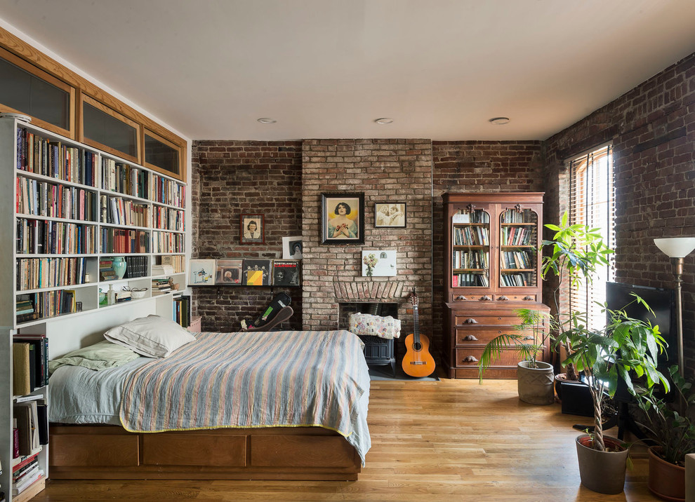 Small industrial bedroom in New York with light hardwood floors, a wood stove and a brick fireplace surround.