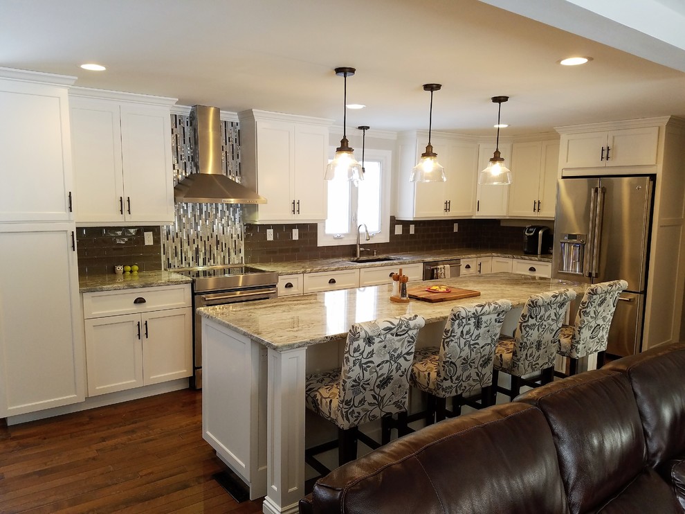 Example of a large transitional galley medium tone wood floor and brown floor open concept kitchen design with an undermount sink, raised-panel cabinets, white cabinets, granite countertops, brown backsplash, ceramic backsplash, stainless steel appliances and an island