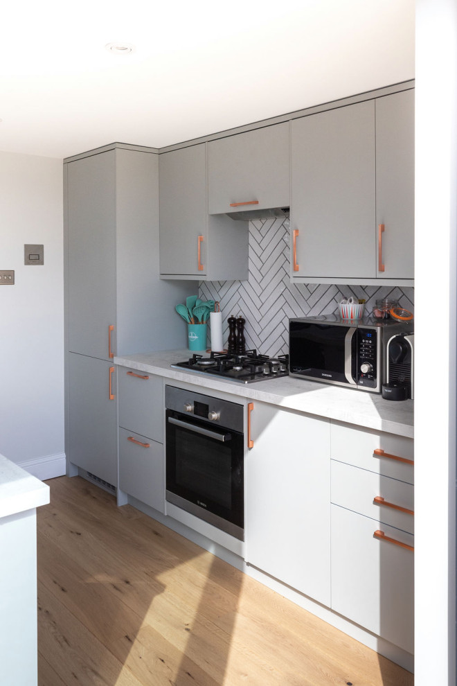 На фото: параллельная кухня-гостиная среднего размера: освещение в стиле модернизм с серыми фасадами, белым фартуком, фартуком из керамической плитки, темным паркетным полом, островом и коричневым полом