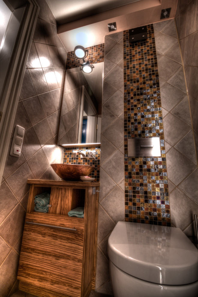 Cette image montre un petit WC suspendu traditionnel en bois brun avec un placard à porte plane, un carrelage beige, mosaïque, un mur beige, un sol en carrelage de céramique, une vasque, un plan de toilette en verre, un sol beige, un plan de toilette marron, meuble-lavabo suspendu et un plafond décaissé.
