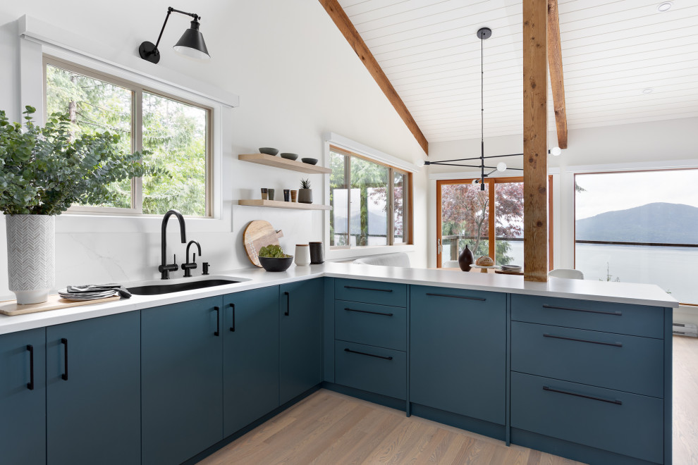 Mid-sized midcentury l-shaped eat-in kitchen in Vancouver with an undermount sink, flat-panel cabinets, blue cabinets, quartz benchtops, white splashback, engineered quartz splashback, stainless steel appliances, light hardwood floors, a peninsula, beige floor, white benchtop and exposed beam.
