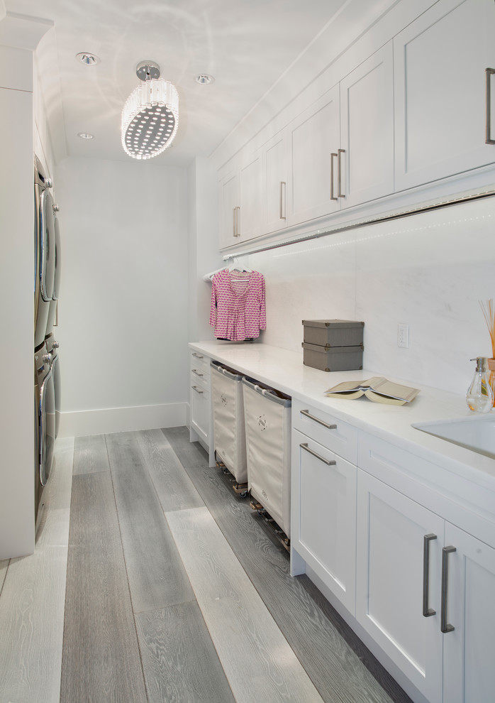 Photo of a transitional galley laundry room in Miami with shaker cabinets, white cabinets, a stacked washer and dryer, white walls and light hardwood floors.