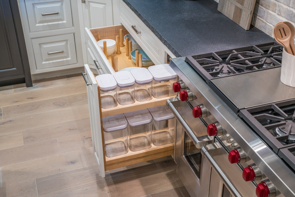 Example of a mid-sized transitional l-shaped medium tone wood floor and brown floor eat-in kitchen design in San Francisco with a farmhouse sink, raised-panel cabinets, white cabinets, granite countertops, white backsplash, marble backsplash, stainless steel appliances, an island and black countertops