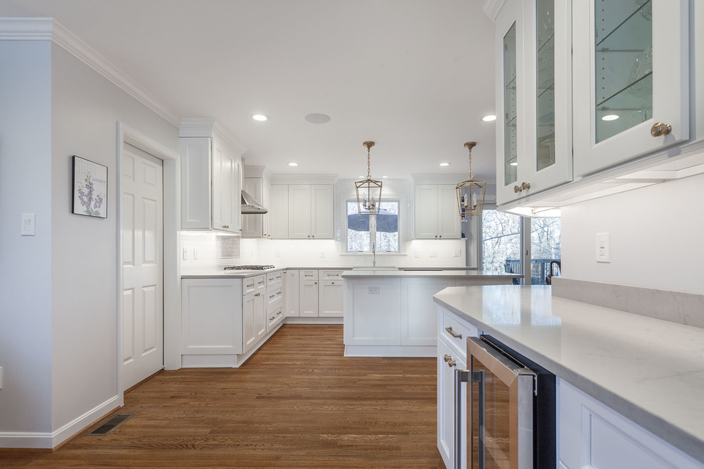 Photo of a large country l-shaped open plan kitchen in DC Metro with a farmhouse sink, shaker cabinets, white cabinets, quartz benchtops, white splashback, ceramic splashback, stainless steel appliances, medium hardwood floors, with island, brown floor and yellow benchtop.