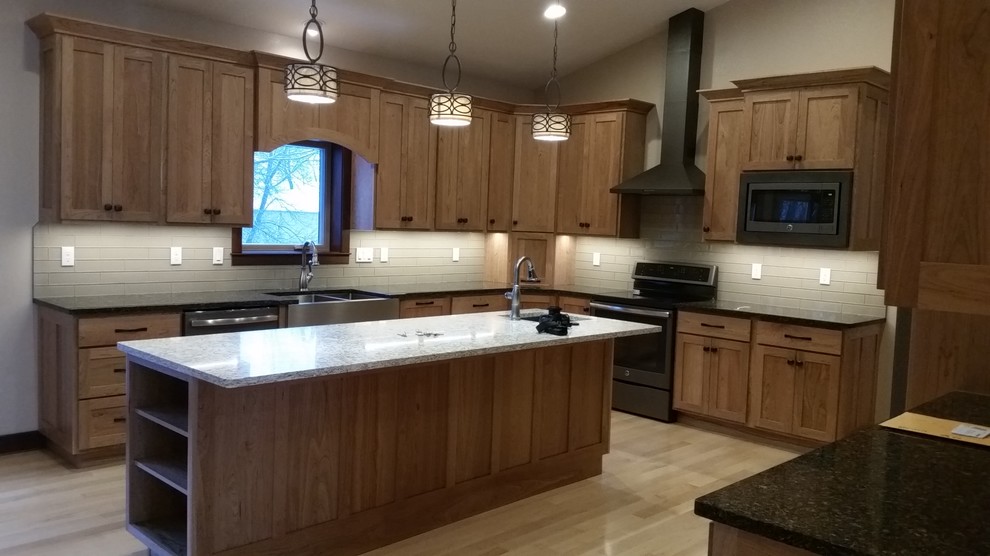 Open concept kitchen - large transitional u-shaped light wood floor and beige floor open concept kitchen idea with a farmhouse sink, shaker cabinets, medium tone wood cabinets, quartzite countertops, gray backsplash, stainless steel appliances and an island
