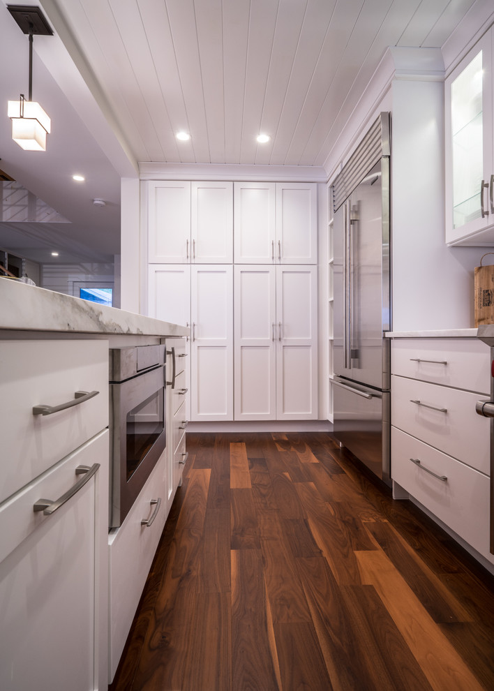 Photo of a mid-sized transitional u-shaped kitchen pantry in Burlington with a farmhouse sink, shaker cabinets, white cabinets, marble benchtops, stone slab splashback, stainless steel appliances, dark hardwood floors and with island.