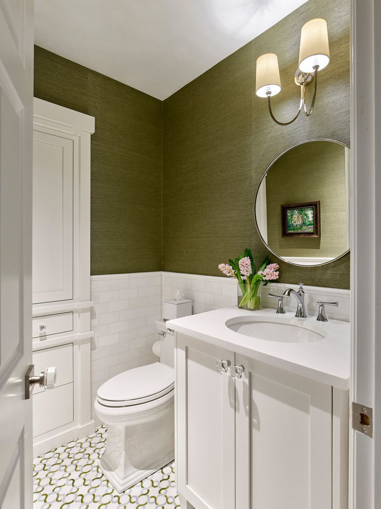 Inspiration for a mid-sized transitional powder room in Philadelphia with white cabinets, a one-piece toilet, white tile, ceramic tile, green walls, mosaic tile floors, an undermount sink, solid surface benchtops, white benchtops, shaker cabinets and multi-coloured floor.