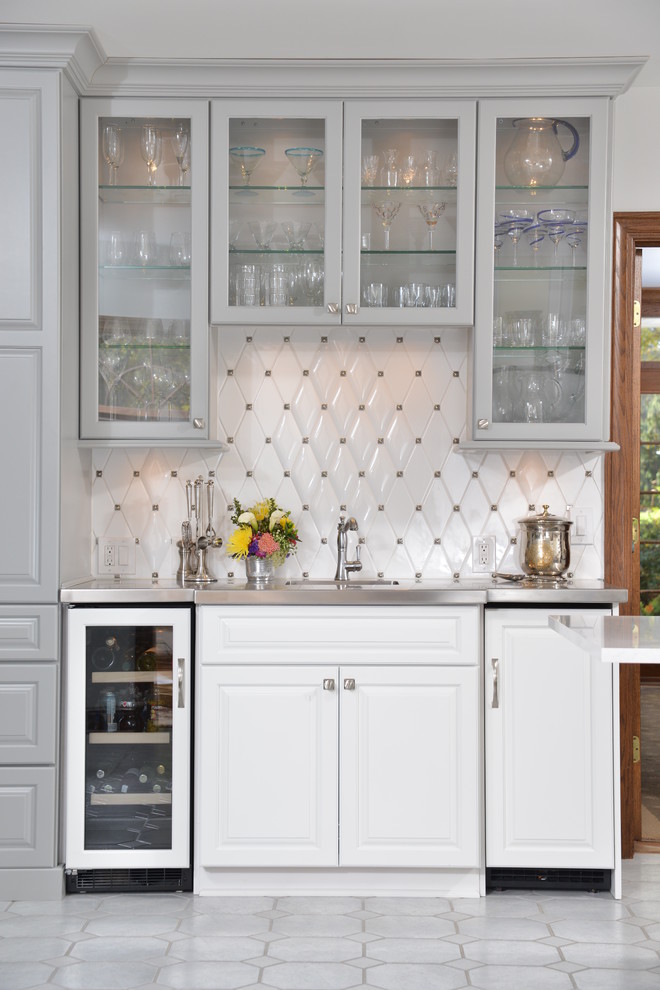 Photo of a traditional single-wall wet bar in Cleveland with glass-front cabinets, white cabinets, white splashback, stainless steel benchtops and white floor.