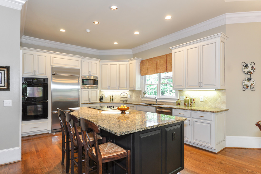 Photo of a mid-sized traditional l-shaped eat-in kitchen in Atlanta with a drop-in sink, raised-panel cabinets, white cabinets, concrete benchtops, beige splashback, ceramic splashback, stainless steel appliances, medium hardwood floors and with island.